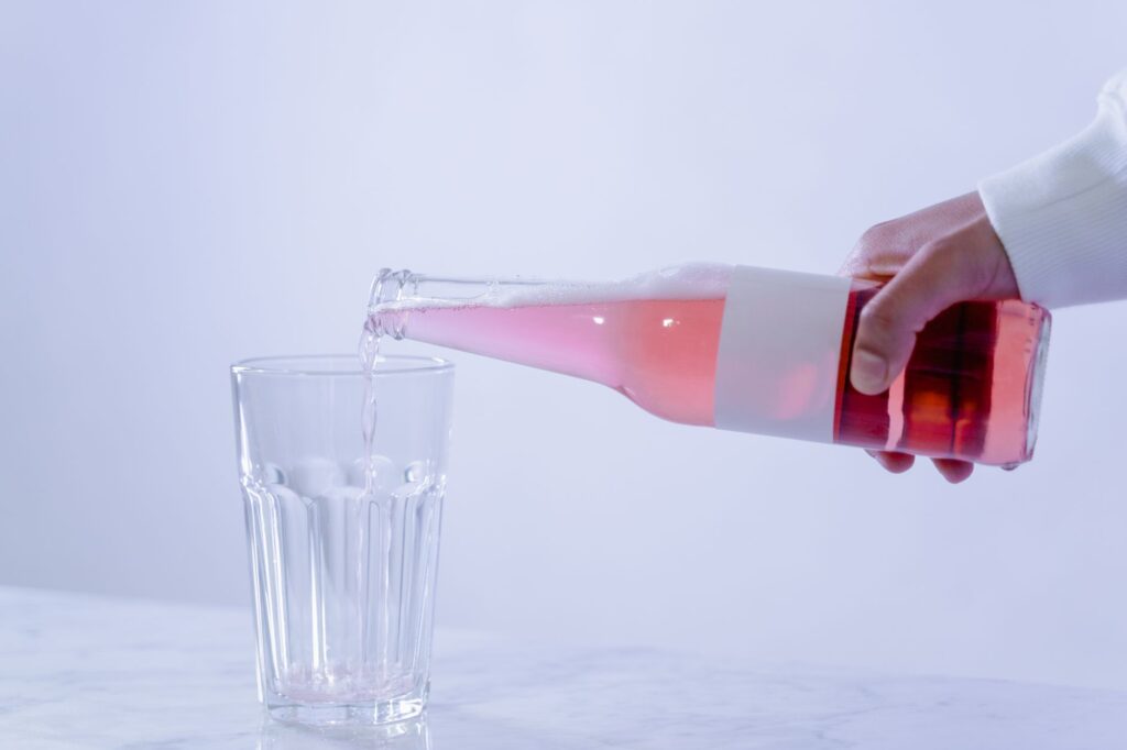 Kombucha being poured from glass bottle into drinking glass on clean kitchen counter