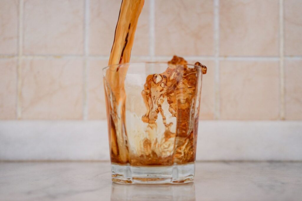 Pouring kombucha from a glass jar on a kitchen counter before a meal