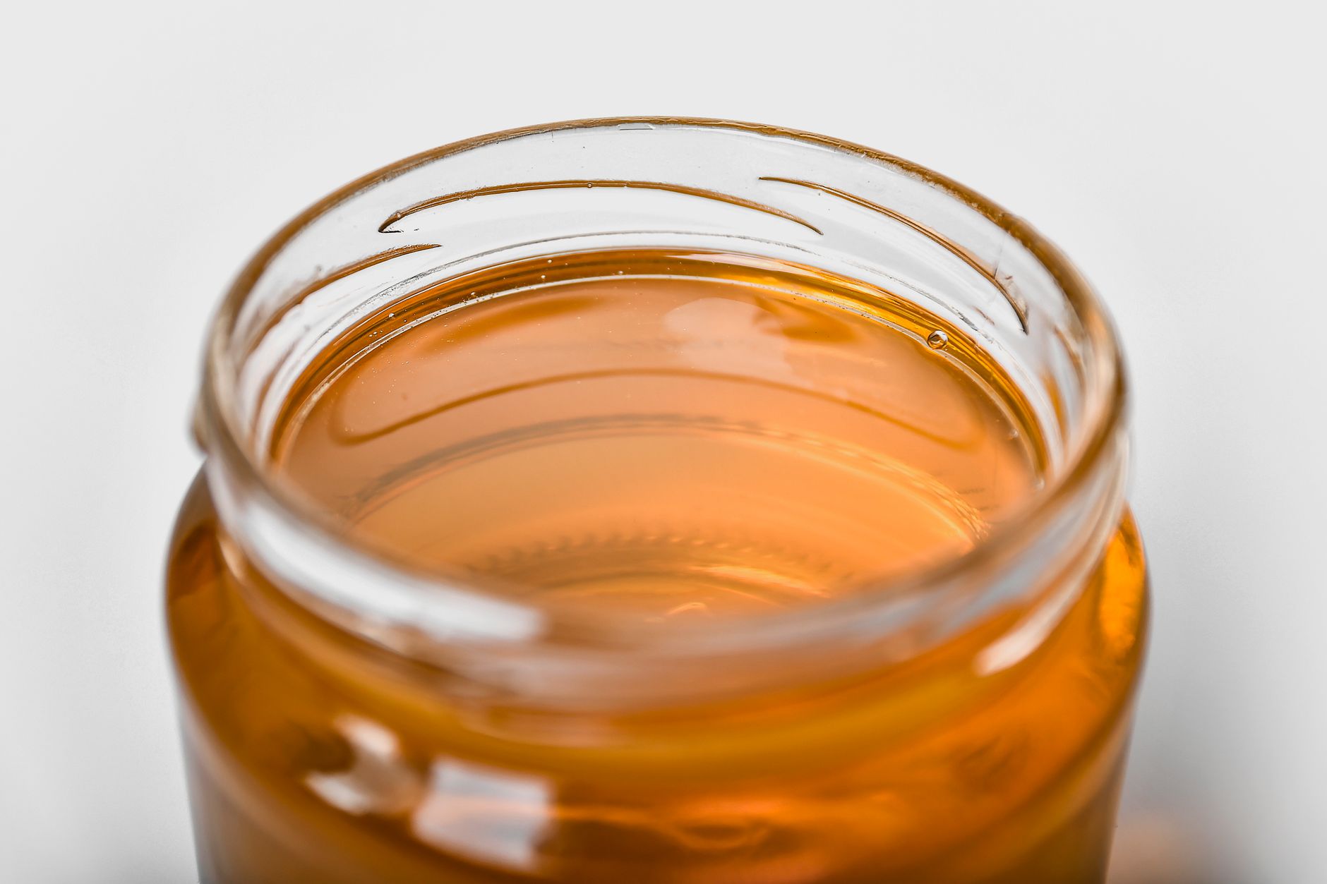 Close up of a glass jar showing kombucha fermenting with a SCOBY culture on a wooden surface.