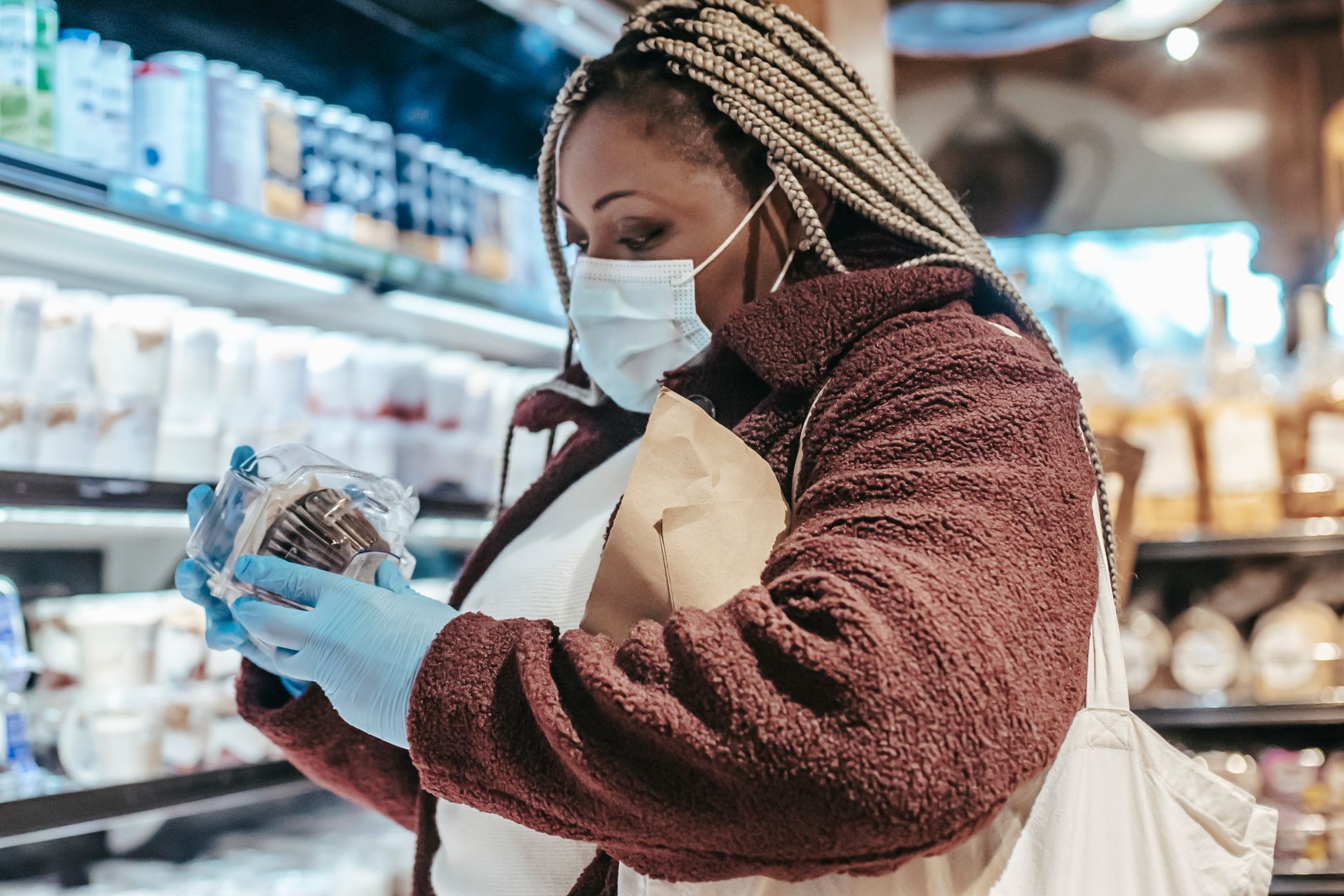 Woman reading a kombucha nutrition label in a grocery store to check sugar and alcohol content before buying.