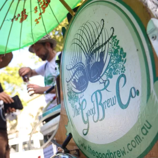 Close-up of the Good Brew Co. logo featuring a stylized bird and plant design on a green background, representing the brand's focus on live fermented kombucha.
