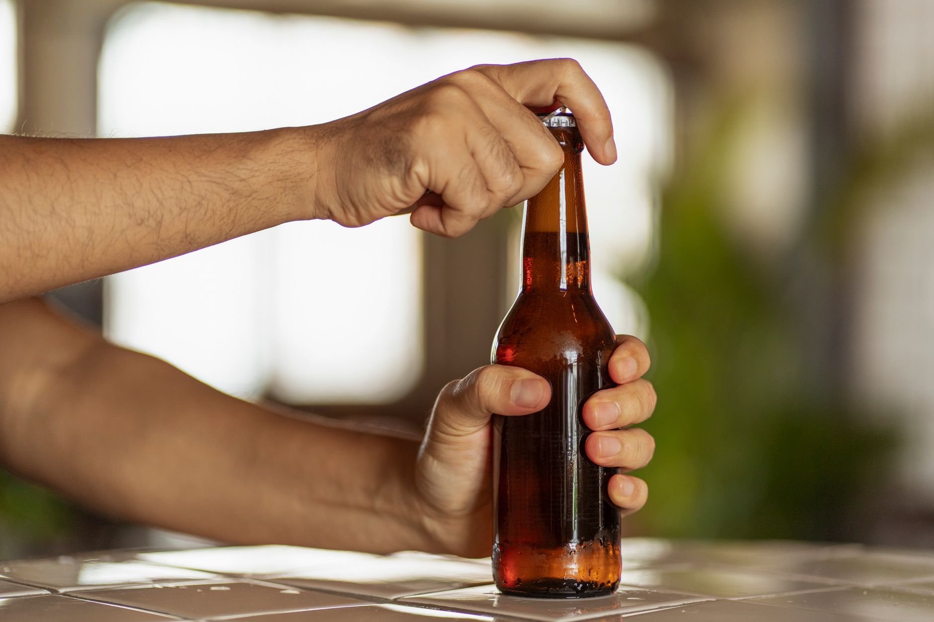 Opened kombucha bottle sitting on a kitchen counter next to a glass ready to pour