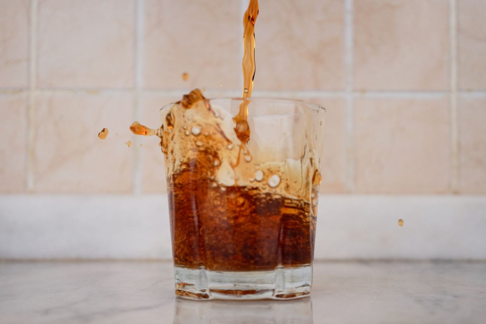 A stream of fizzy kombucha being poured from a bottle into a clear glass showing carbonation bubbles