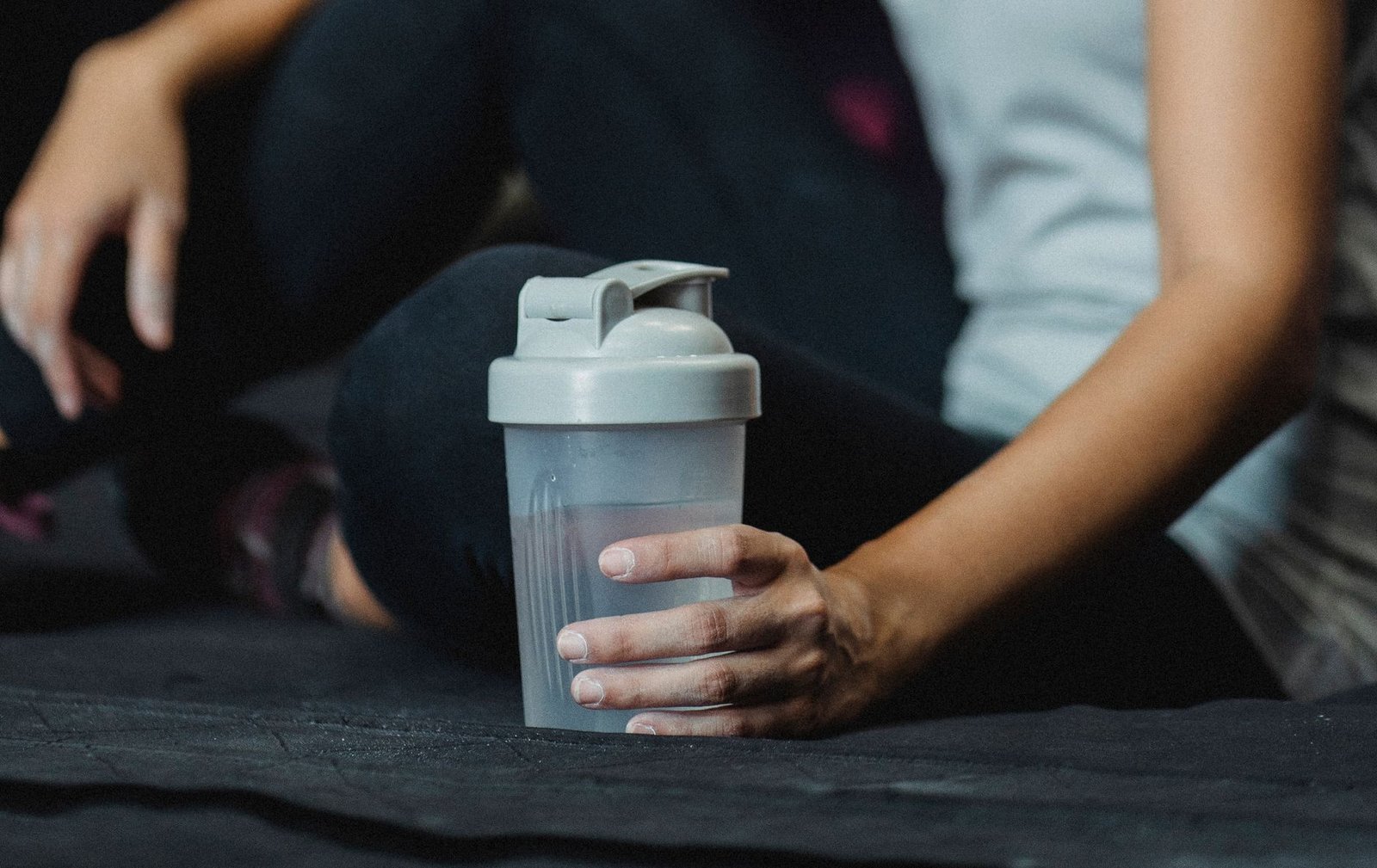 Person holding a cold glass of kombucha after exercise for post-workout recovery