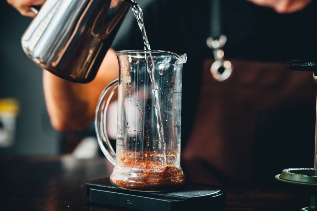 Pouring raw store-bought kombucha as starter liquid into a glass brewing jar on a wooden kitchen counter
